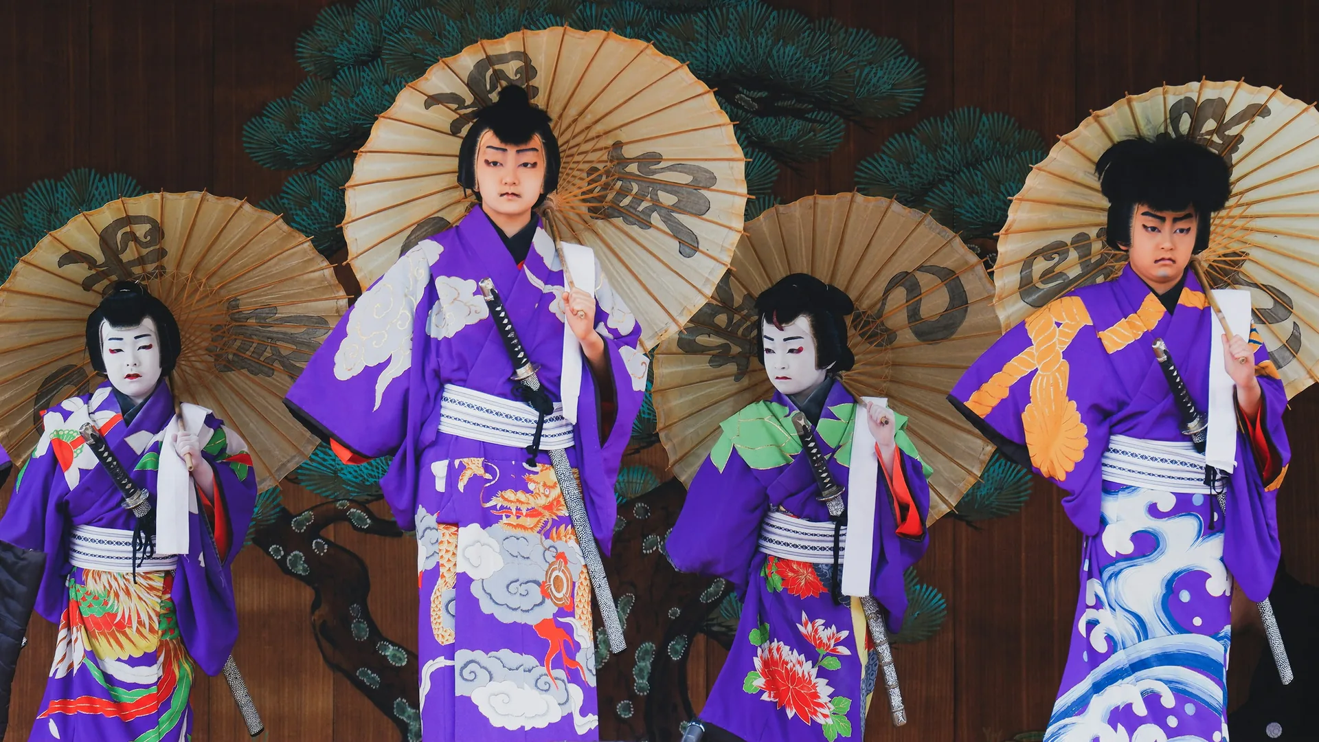 Kabuki performers in colourful kimono and white face makeup on stage before the painted pine backdrop